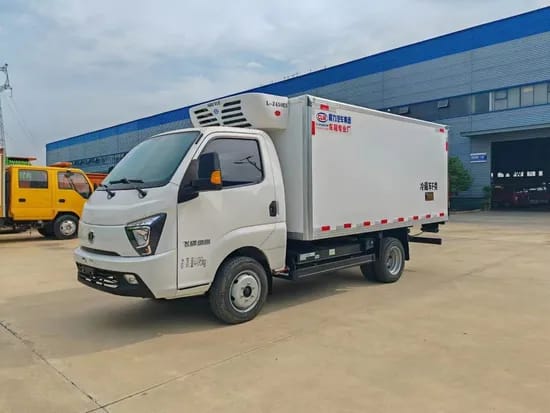 Small white refrigerated truck parked outside a warehouse